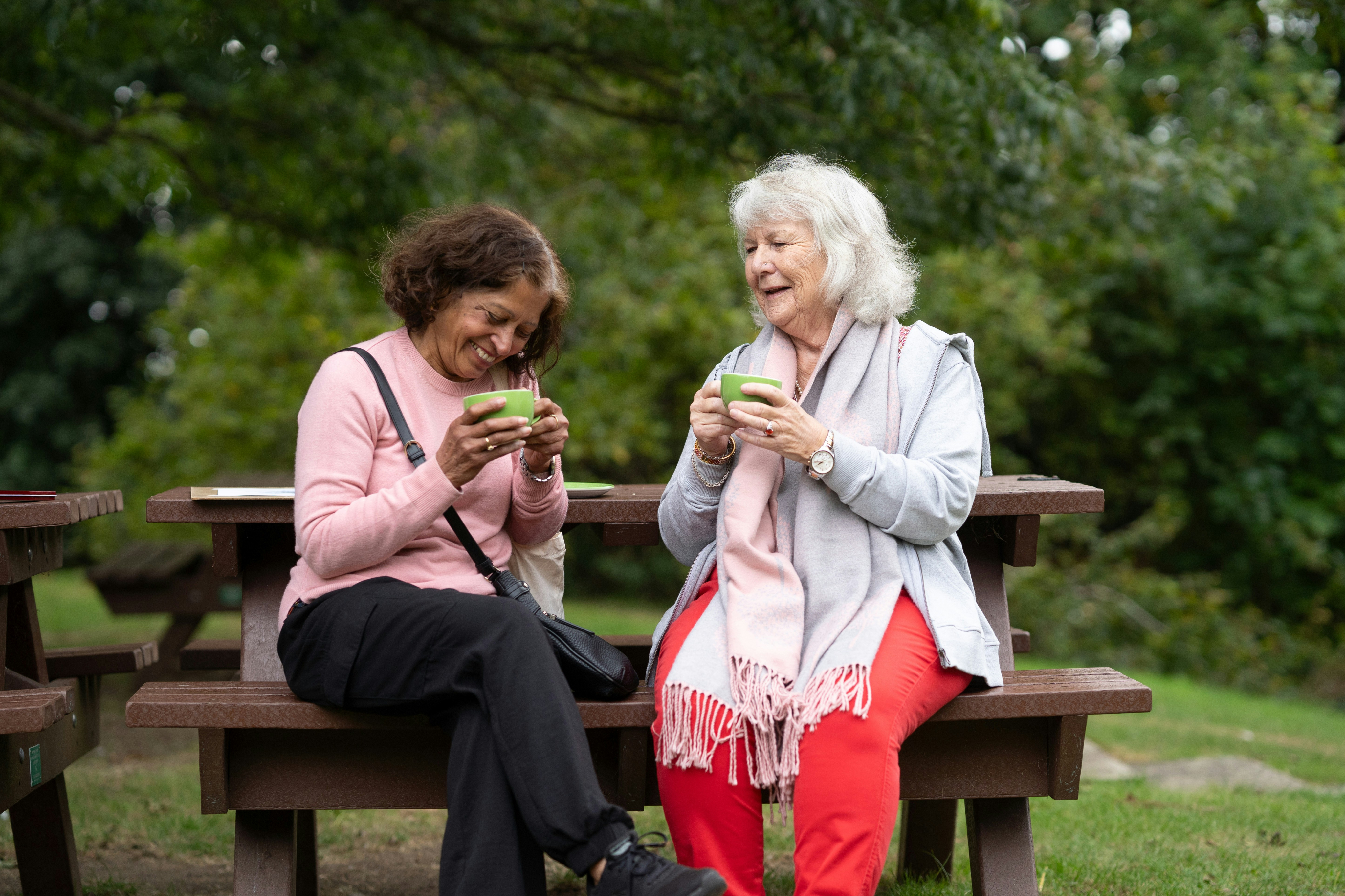 Two women sitting at a modern table talking with a city view behind them.